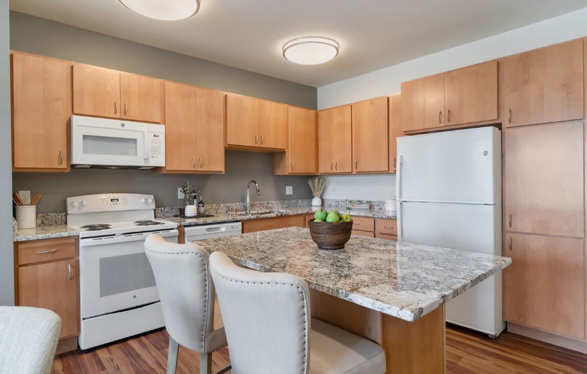 A modern kitchen with wooden cabinetry, marble countertops, and white appliances.