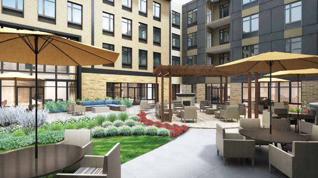 A modern apartment complex courtyard featuring outdoor seating and lush landscaping.