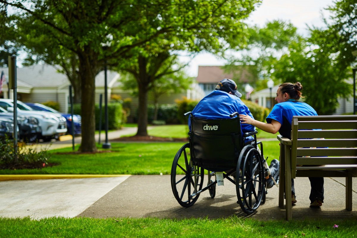 A caregiver assists an elderly person in a wheelchair through a park, showcasing compassion and support.