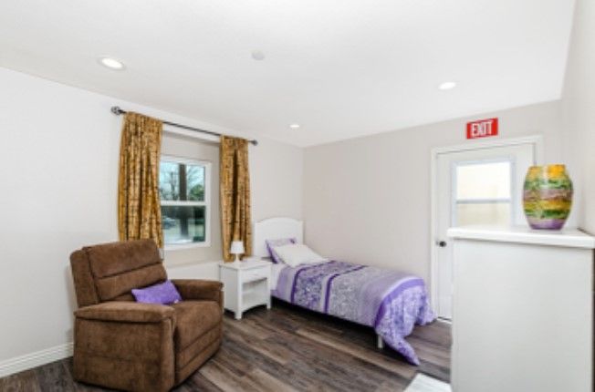 A cozy bedroom with a single bed, armchair, and nightstand in a bright setting.