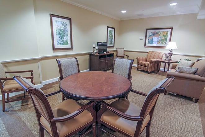 A cozy meeting room with a round table and chairs, decorated with framed paintings and warm colors.