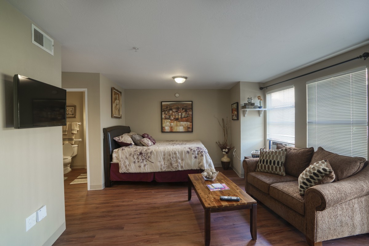 A cozy studio apartment featuring a queen-sized bed, couch, and coffee table with ample natural light.