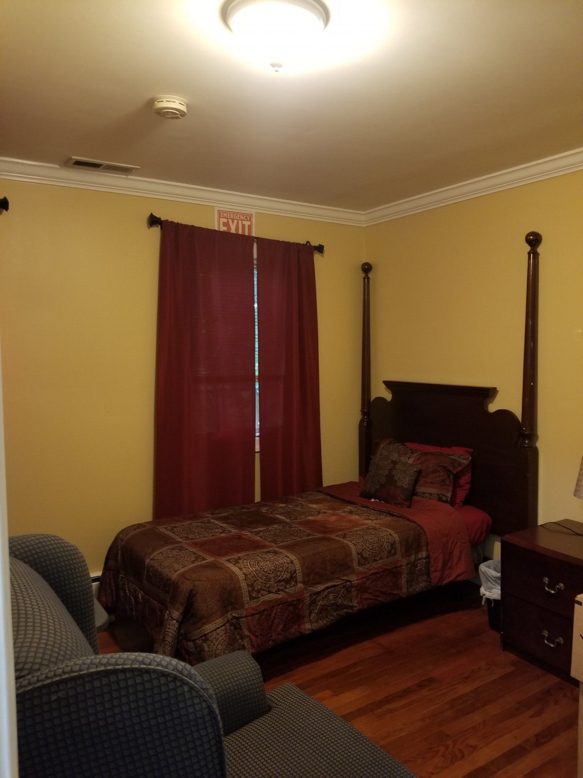 A cozy bedroom with a single bed, dark wood furniture, and yellow walls.