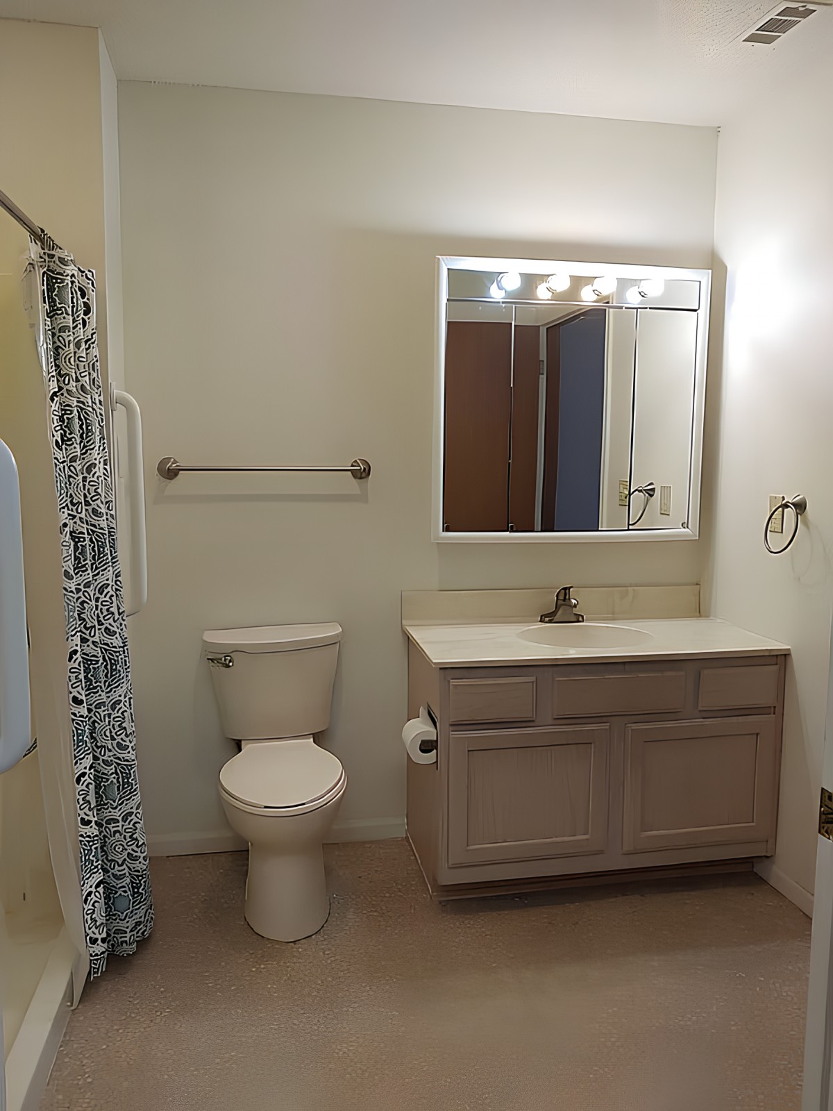 A clean and simple bathroom with a vanity, mirror, toilet, and shower area.