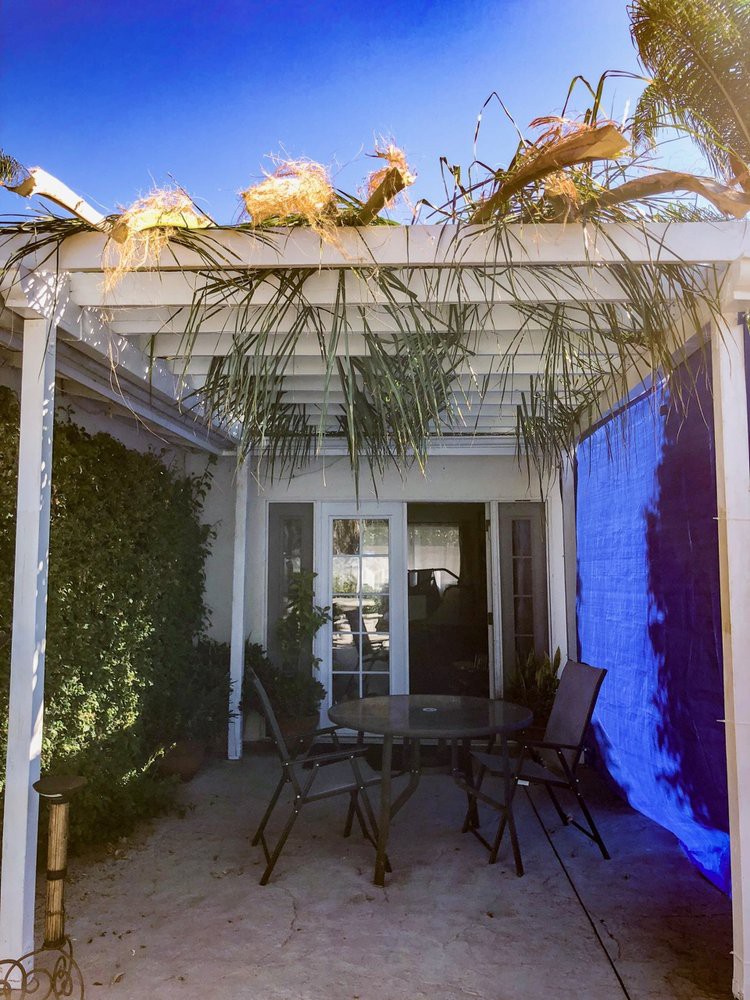 A sunny patio with a pergola, outdoor seating, and surrounding plants.