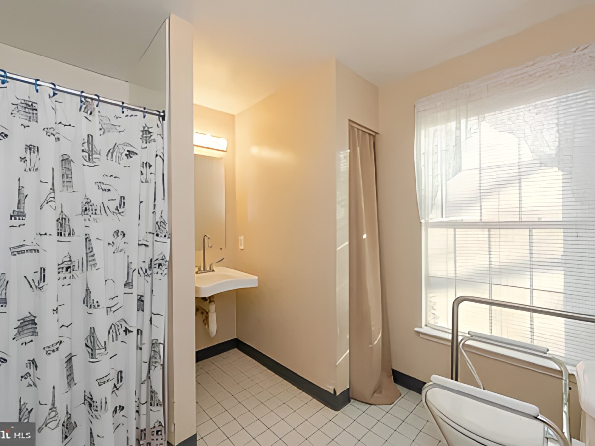 A bright bathroom with a tiled floor, featuring a shower with a curtain, a sink, and a window letting in natural light.