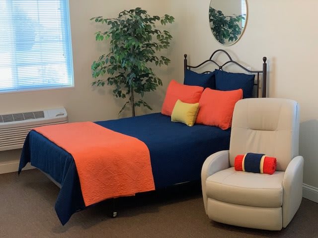 A cozy bedroom with a colorful bedspread, a potted plant, and a comfortable chair.