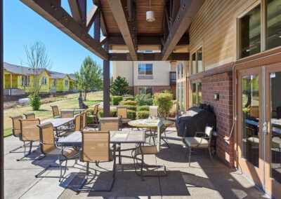 A well-maintained patio with tables, chairs, and a grill under a covered area in a residential setting.