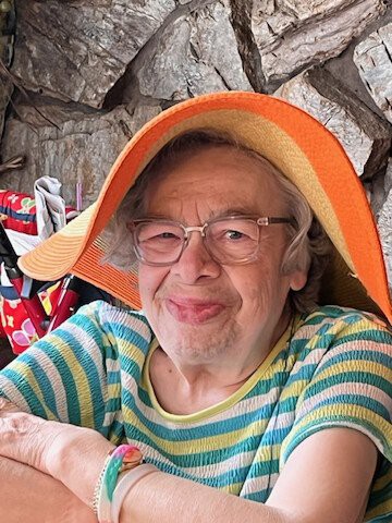 An elderly woman wearing an orange hat and a striped shirt, smiling at the camera.