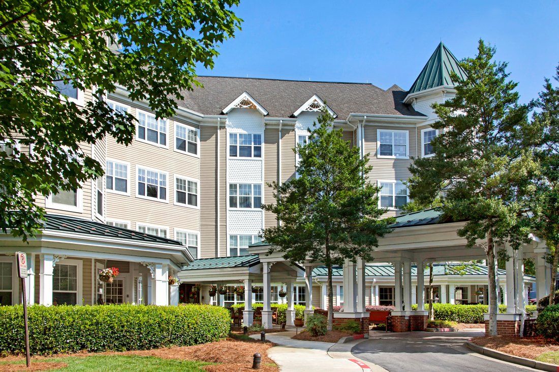A large, multi-story residential building with a landscaped entrance and trees on a sunny day.