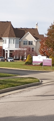A view of a residential building with a sign in front, framed by landscaped lawns and trees.
