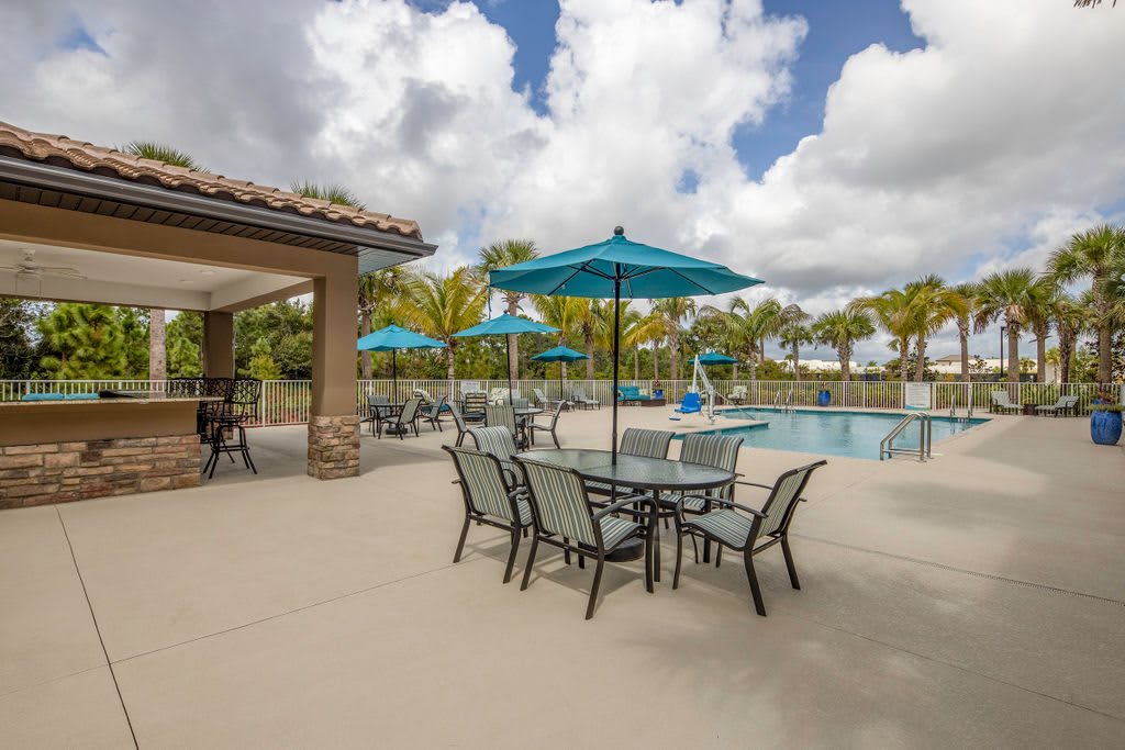 Outdoor poolside area with tables, chairs, and umbrellas on a sunny day.