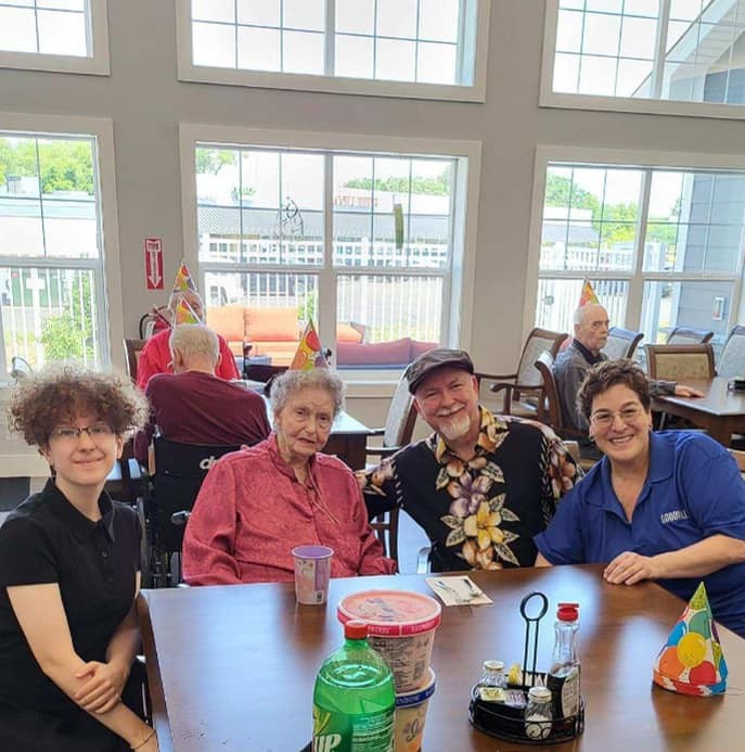 A group of people enjoying a celebration indoors, wearing party hats and smiling around a table.