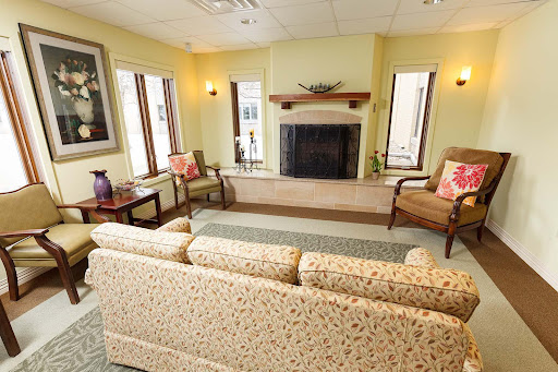 A cozy living room featuring a sofa, chairs, and a fireplace, illuminated by natural light.