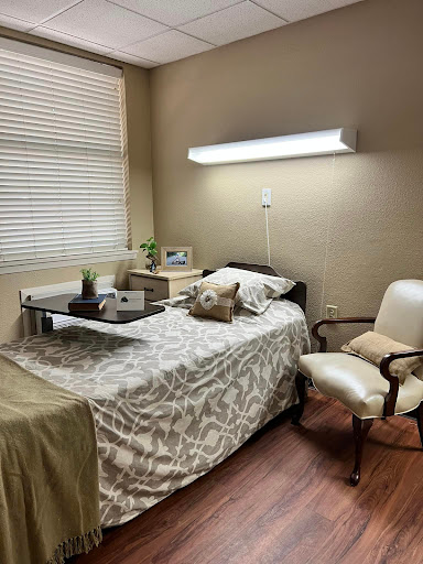 A cozy hospital room featuring a neatly made bed, a small table with decorative items, and comfortable seating.