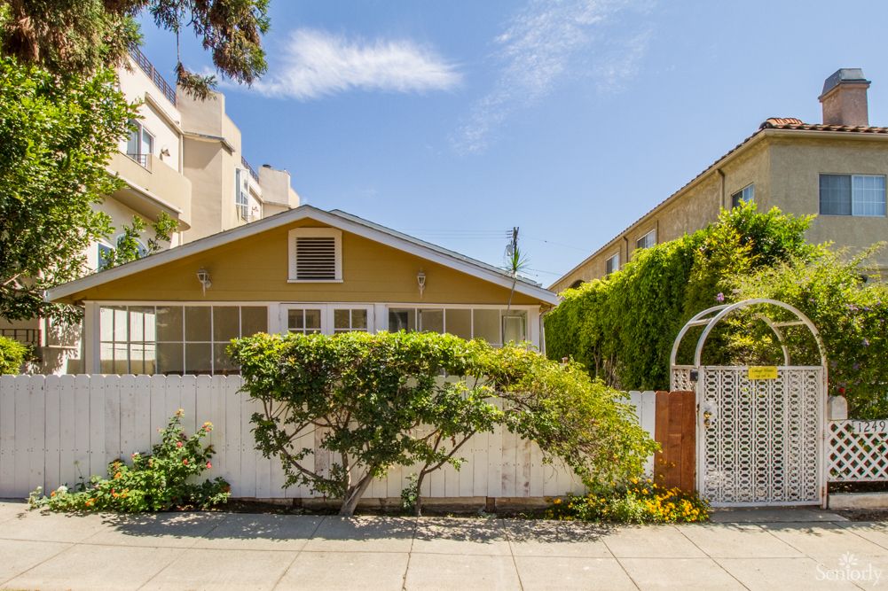 A charming suburban house with a white fence and greenery under a clear blue sky.