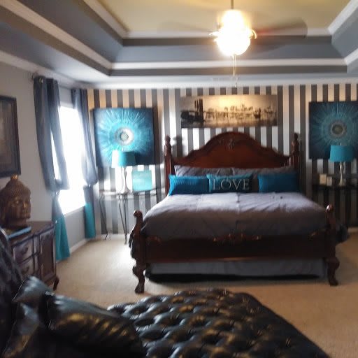A well-decorated bedroom featuring a wooden bed, striped wallpaper, and a ceiling fan.