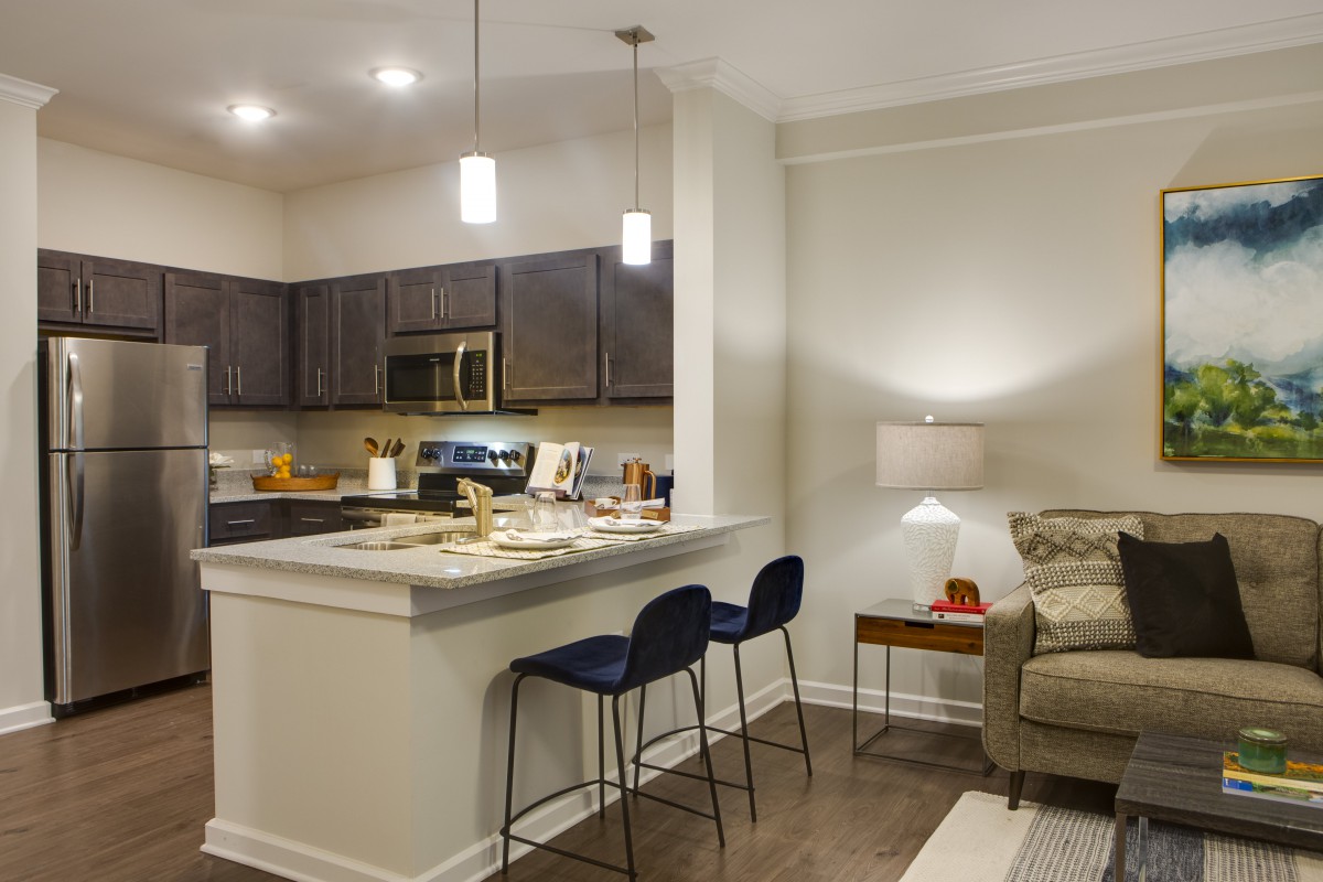 A modern apartment with an open-layout kitchen and living room featuring pendant lights and counter stools.