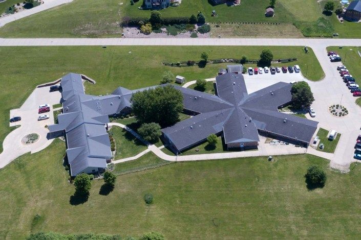 Aerial view of a uniquely shaped building with surrounding green landscape and parking area.