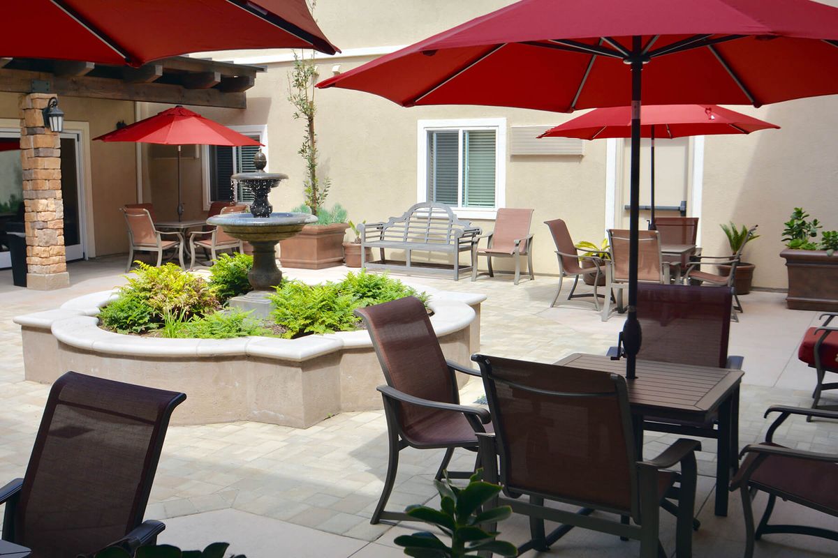 A serene patio area with seating, red umbrellas, and a central fountain surrounded by greenery.