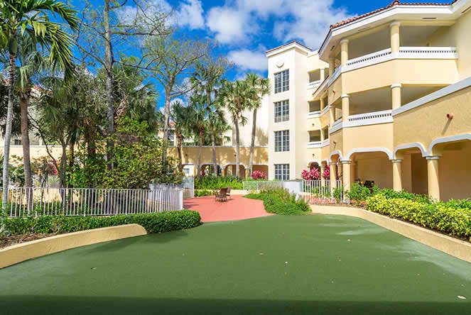 A sunny courtyard within a residential apartment complex, featuring well-maintained landscaping and lush greenery.