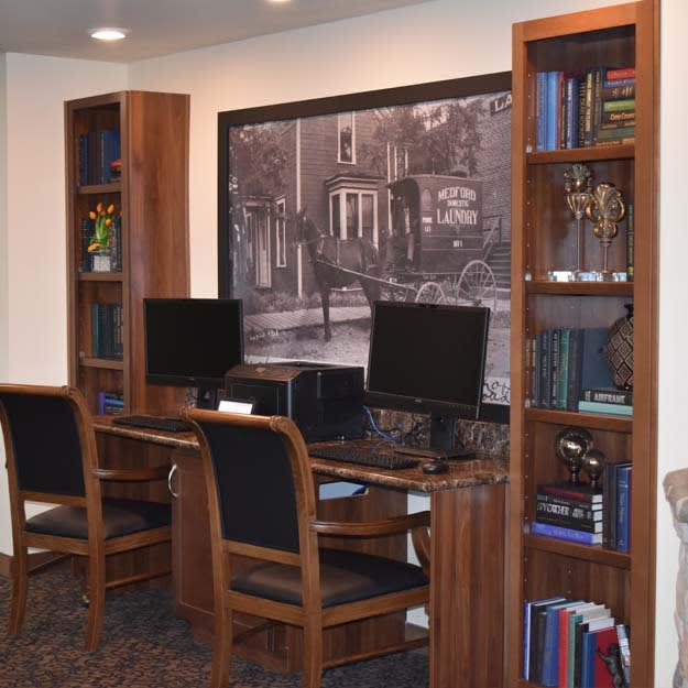 A cozy office space with computers, wooden chairs, and bookshelves.