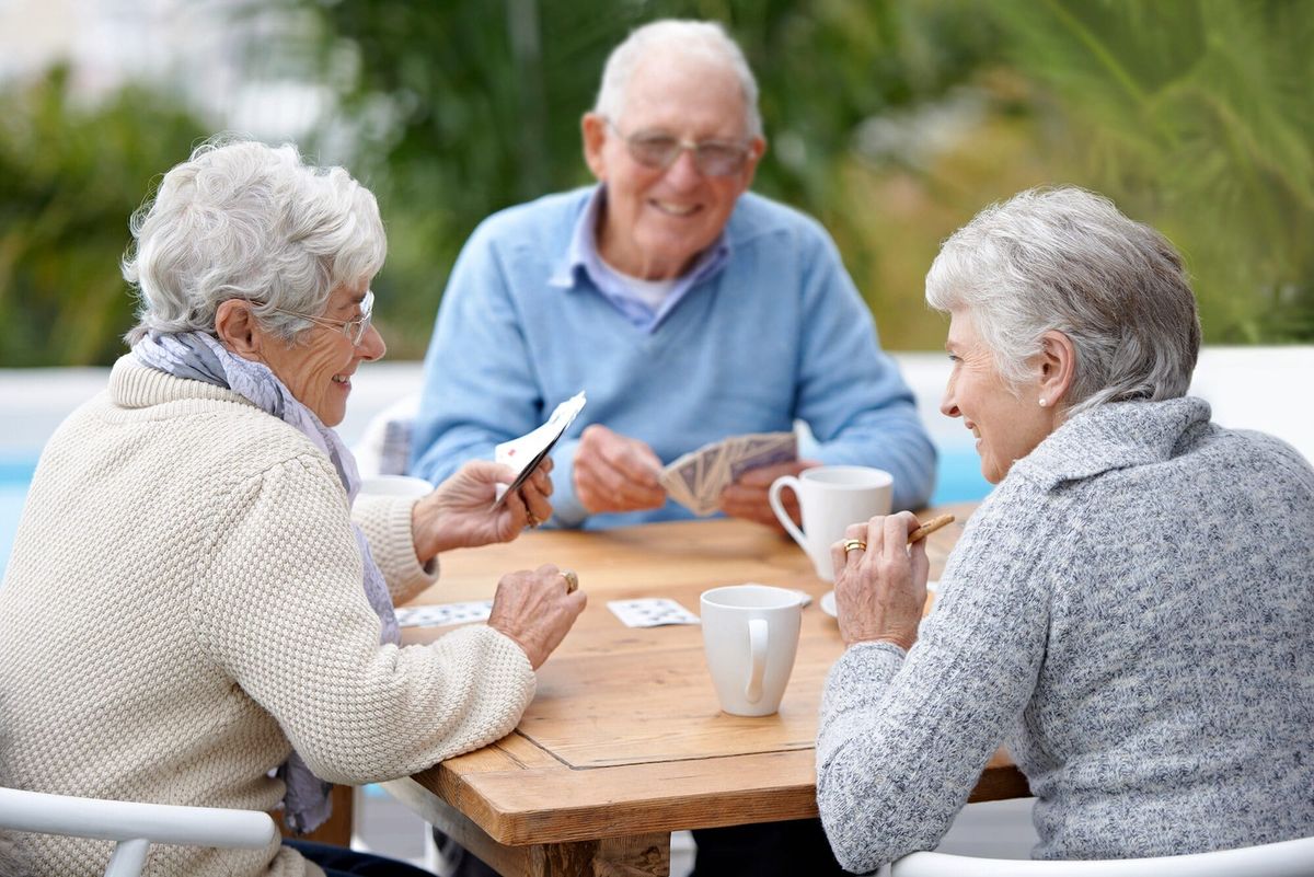 A group of senior friends enjoying a card game outdoors.