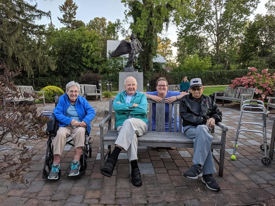 A group of four people sitting together on a bench in a garden setting.