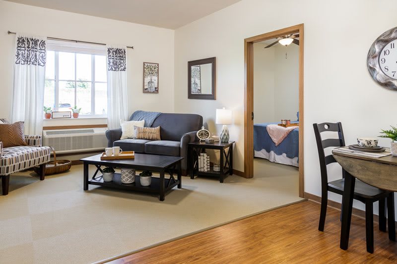 A cozy living room with soft lighting, featuring a sofa and coffee table, adjacent to a bedroom.