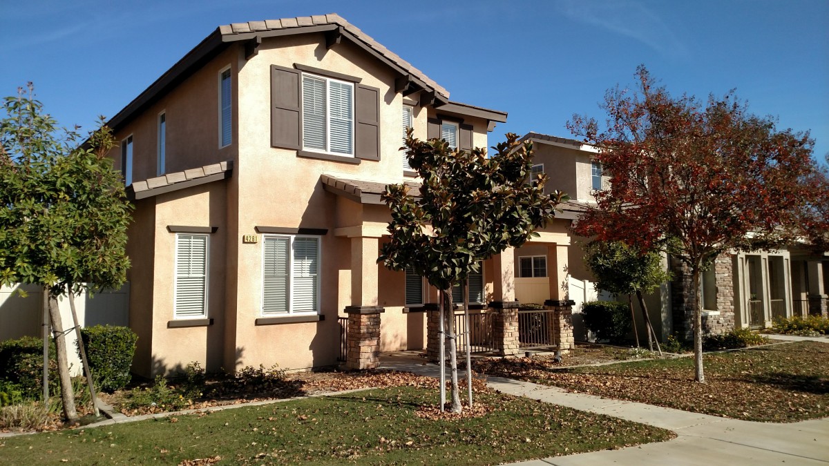 A suburban house with a small tree in front, set under a clear blue sky on an autumn day.