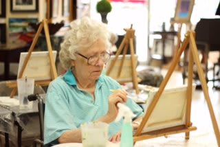 An elderly woman engaged in painting during an art class.