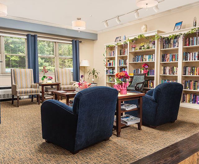 A cozy library room featuring comfortable armchairs, bookshelves filled with books, and large windows letting in natural light.