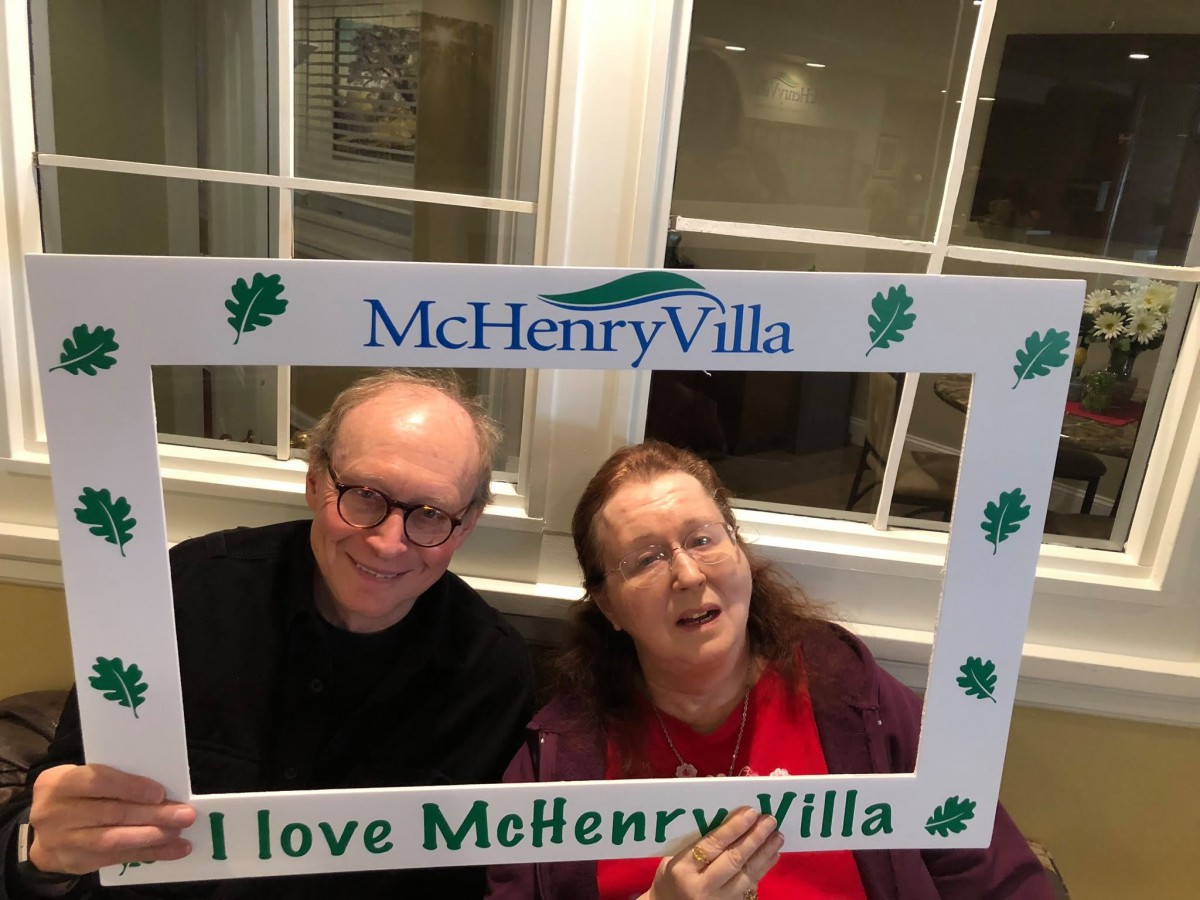 Two people smiling while holding a McHenry Villa photo frame indoors.