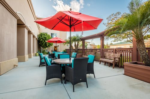 A sunny outdoor patio with red umbrellas and comfortable garden furniture.
