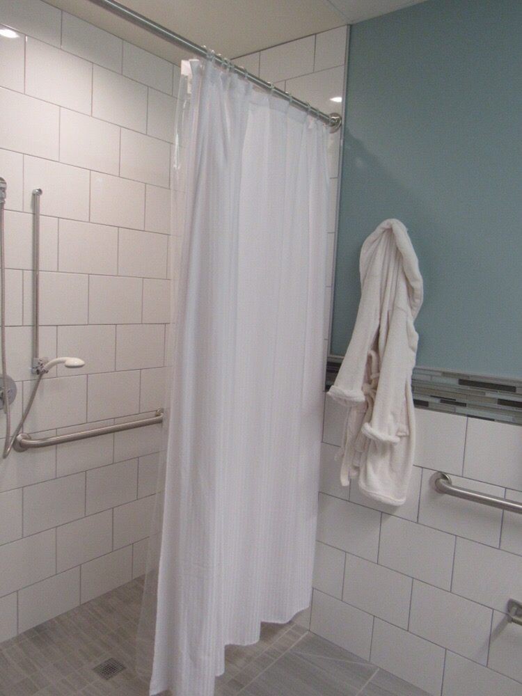 A bathroom featuring a shower with a white curtain, tiled walls, and safety handrails.