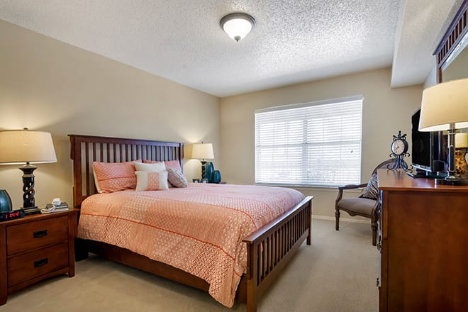 A cozy bedroom with a wooden bed, bedside lamp, and a window letting in natural light.