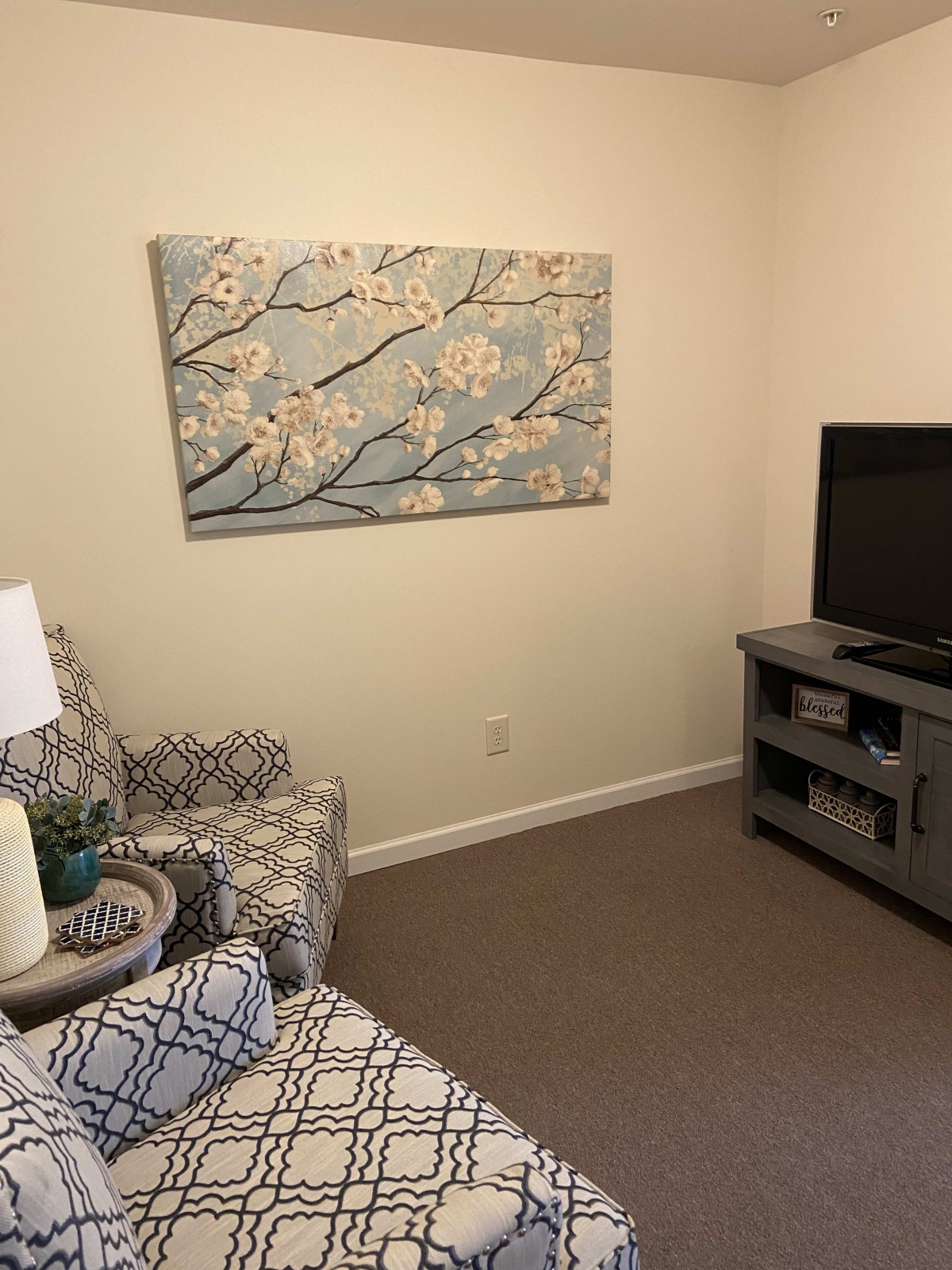 A cozy living room with patterned armchair, wall art, and a television on a stand.