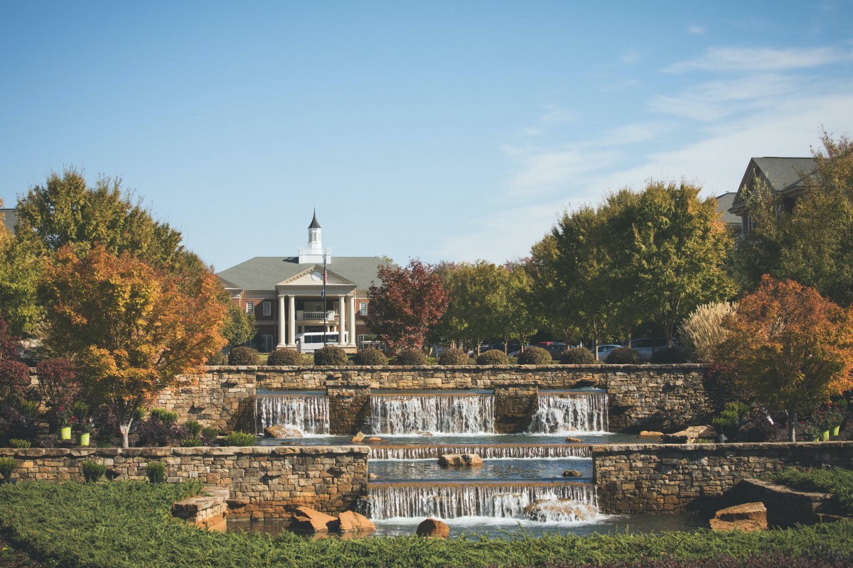 A picturesque garden scene featuring a multi-tiered stone waterfall with autumn foliage in the background.
