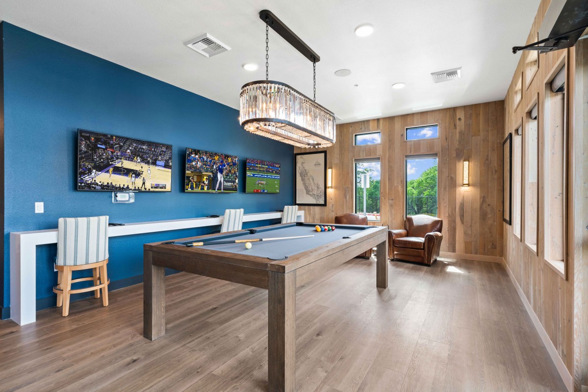 A modern game room featuring a pool table, stylish chandelier, and comfortable seating with large windows.