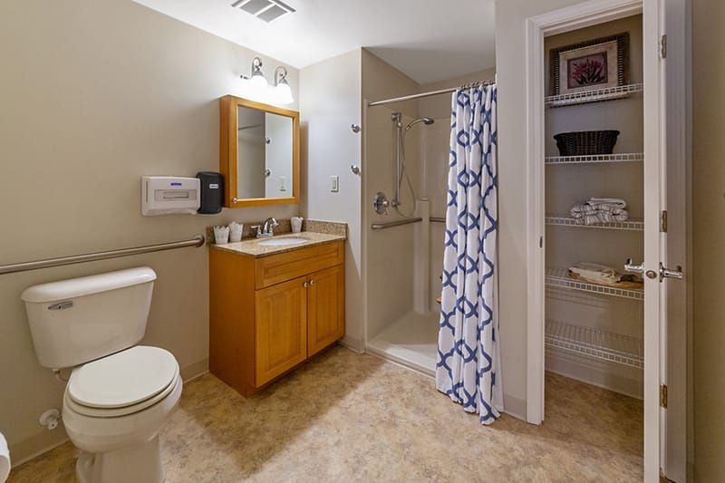 A clean and organized bathroom featuring a shower with a patterned curtain, a wooden vanity with a mirror, and a tiled floor.