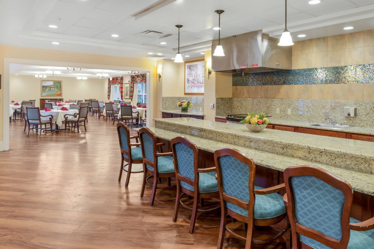A spacious dining and kitchen area with a long counter and several chairs, featuring elegant lighting and wood flooring.