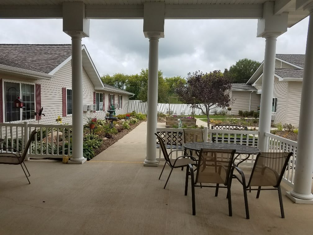 A covered patio with outdoor seating overlooking a landscaped garden area between residential buildings.