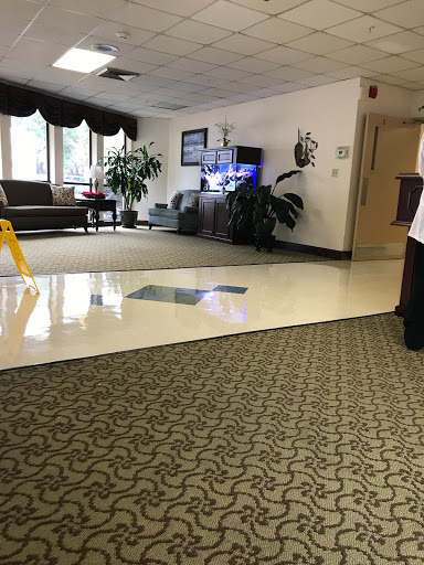 A spacious indoor lobby with seating, plants, and a television, featuring caution signage on the floor.