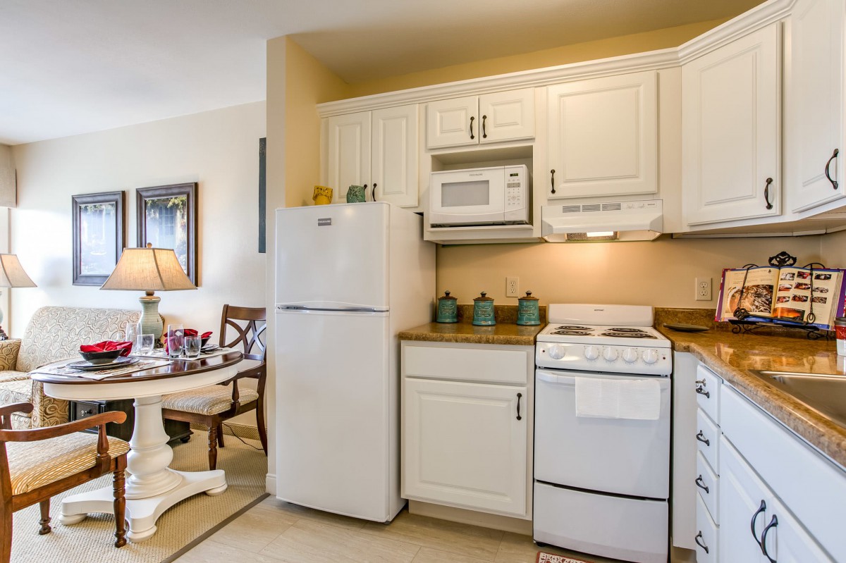 A cozy kitchen with white cabinets and appliances, featuring a refrigerator, stove, and microwave next to a dining area.