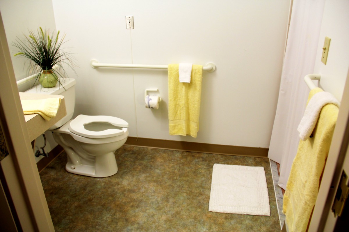 A tidy bathroom with a toilet, yellow towels, and a white floor mat.