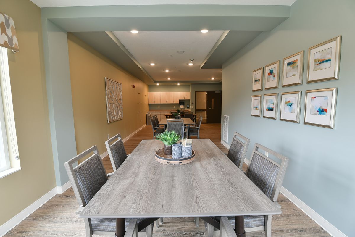 A modern dining room with a view into the kitchen, featuring a stylish table and chairs set, tasteful decor, and ambient lighting.