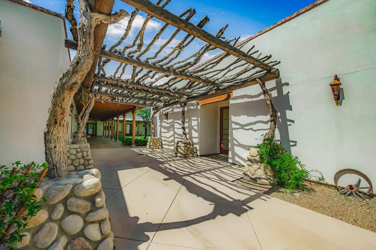 A sunny outdoor area with a wooden pergola and stone pillars casting intricate shadows on the ground.