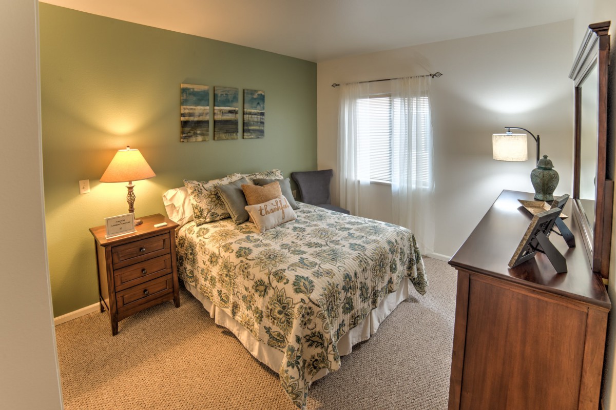 A cozy bedroom featuring a patterned bedspread, bedside tables with lamps, and wall art above the bed.