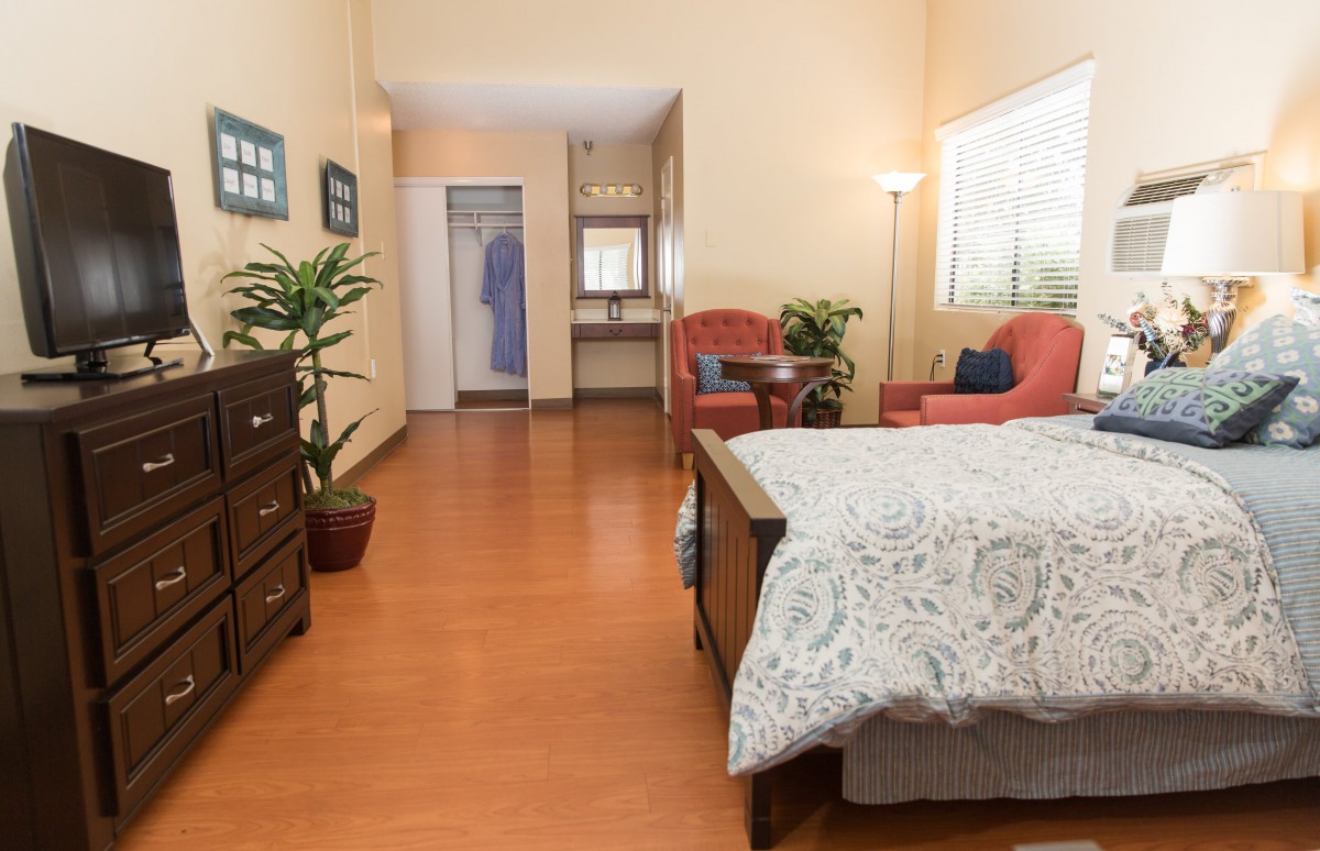 A cozy bedroom with a bed, armchairs, plants, and wooden flooring.