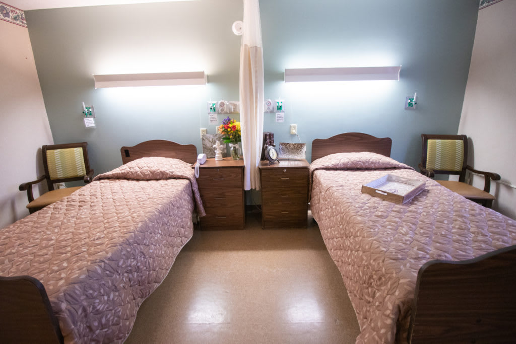 A clean hospital room with two single beds, bedside tables, and soft lighting.